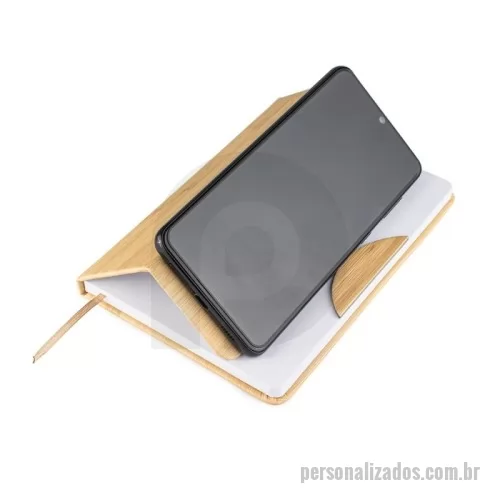 Caderno ecológico personalizado - A caderneta feita para quem valoriza praticidade com um toque de estilo. Feita em plástico, sua capa se assemelha ao charme natural do bambu, chamando a atenção em qualquer lugar. Internamente, o marcador de cetim facilita o acesso às anotações, que ganham vida em 80 páginas brancas pautadas, prontas para organizar suas ideias, listas e inspirações. O grande diferencial? O suporte para celular embutido na capa, perfeito para acompanhar vídeos, chamadas e até mesmo reuniões.
