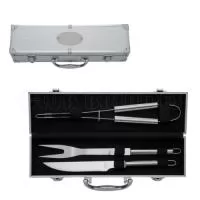 Kit de churrasco com três peças em aço inox, incluindo: um pegador, um garfo e uma faca de corte com lâmina de 6 polegadas. Além disso, os utensílios são acomodados em maleta de alumínio com revestimento interno em TNT e plaquinha para personalização.