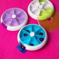 Porta-comprimidos em plástico com design compacto. Possui sete divisórias e um botão de acionamento que gira um compartimento a cada clique, permitindo o acesso ao conteúdo por meio de uma abertura lateral.