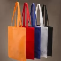 Sacola colorida com alça em material TNT, possui símbolo ecológico/reciclável na costura da alça.
